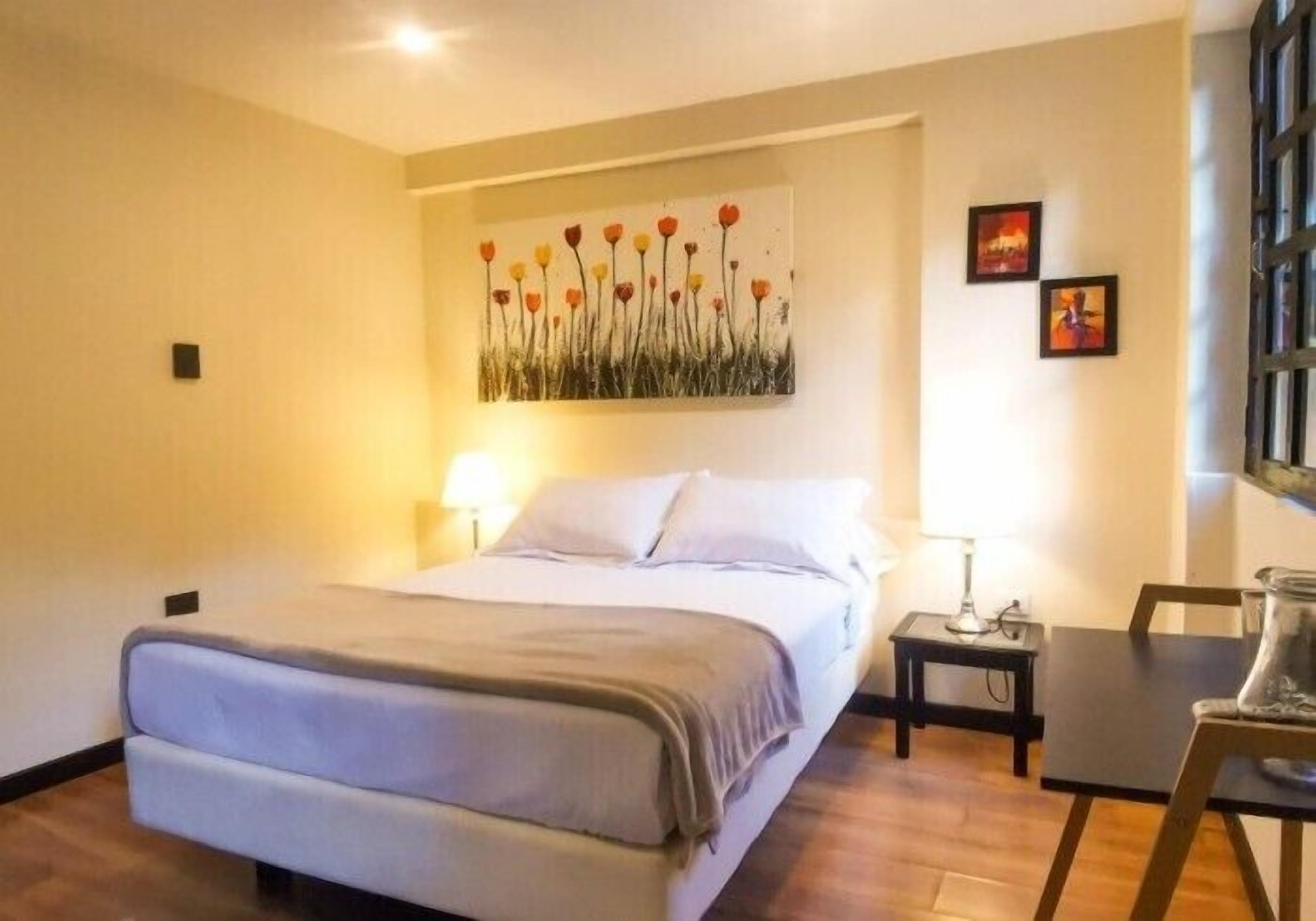 A hotel room with a bed, bedside table, lamp, and artwork on the wall.