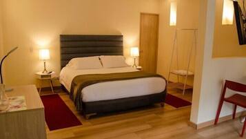 A hotel room with a bed, two bedside tables with lamps, a desk, a chair, and a wooden floor.