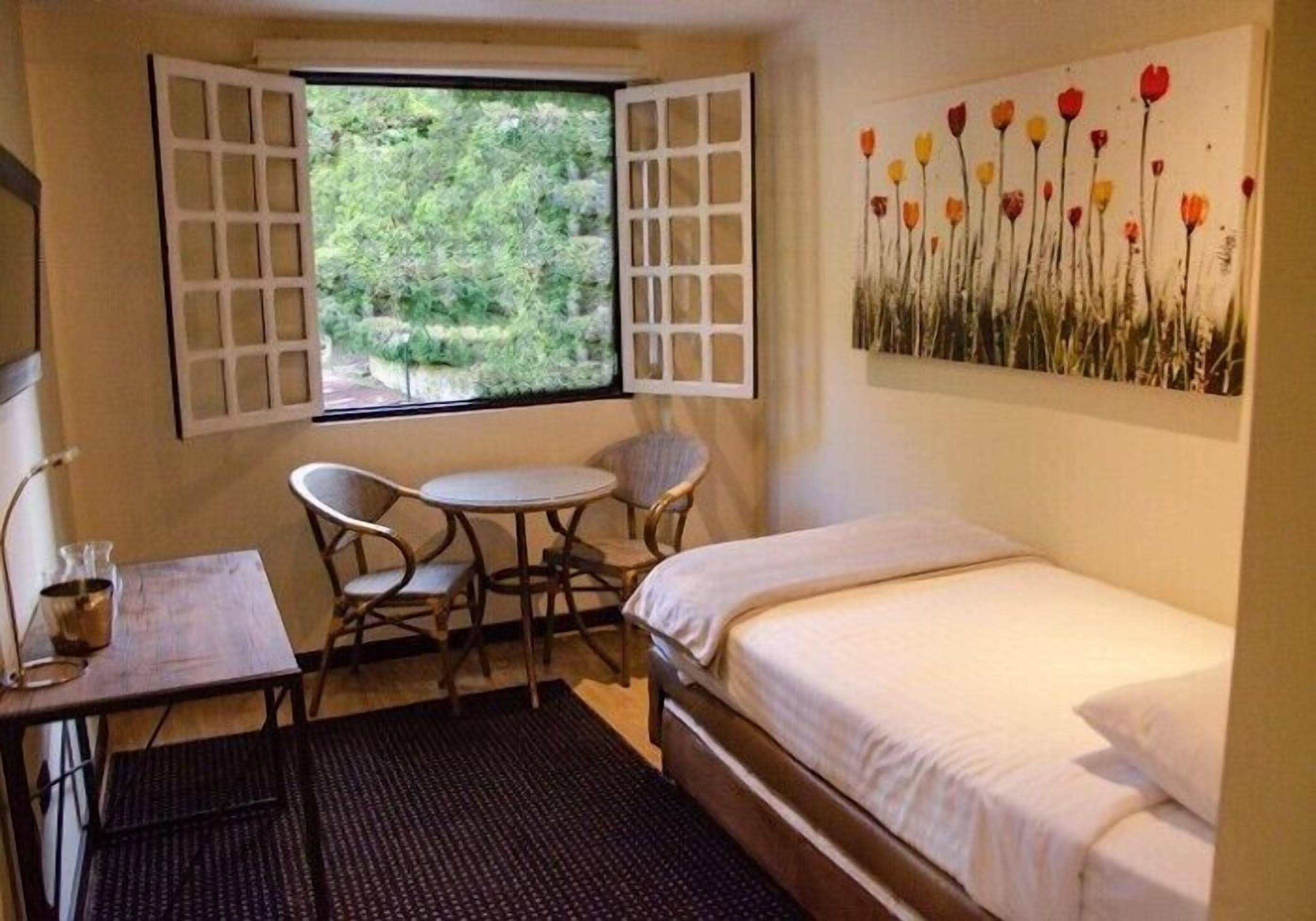 A small room with a bed, a table, two chairs, and a window with open shutters.