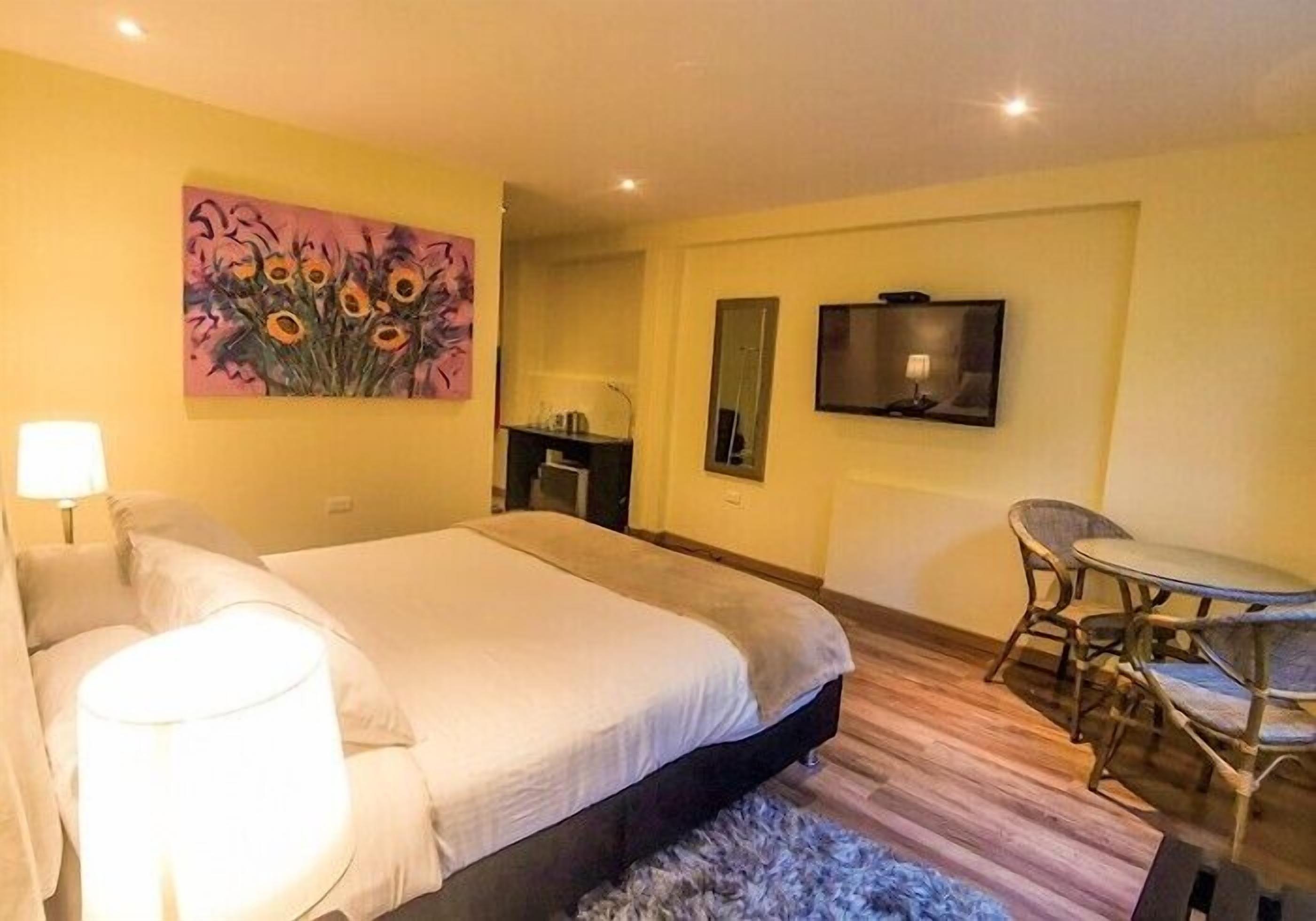A hotel room with a bed, a desk, a chair, a TV, and a painting on the wall.