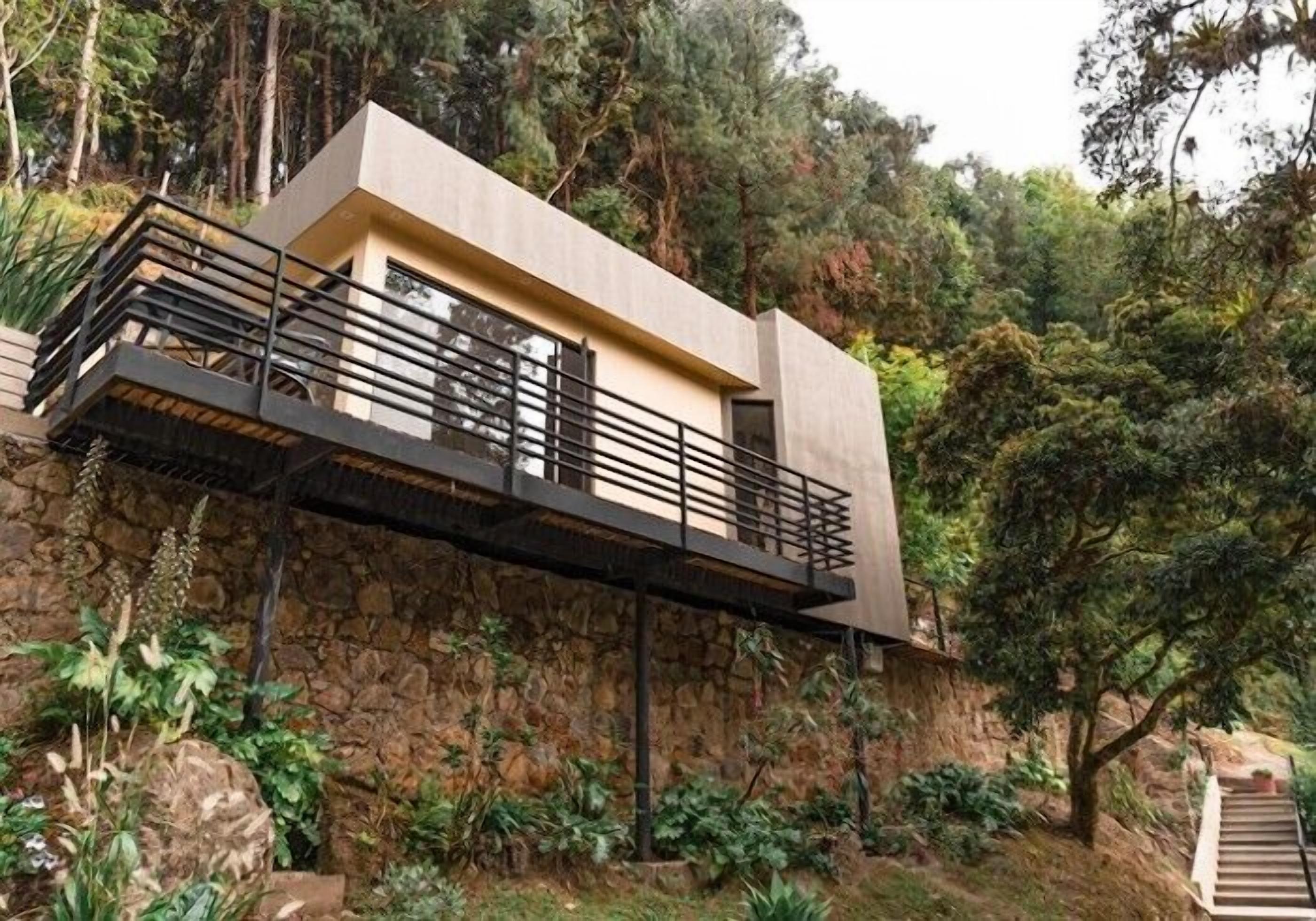 A modern house with a flat roof, a balcony with a metal railing, and a stone wall.