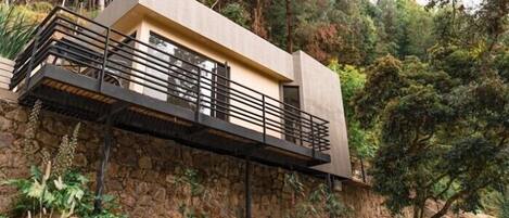 A modern house with a flat roof, a balcony with a metal railing, and a stone wall.