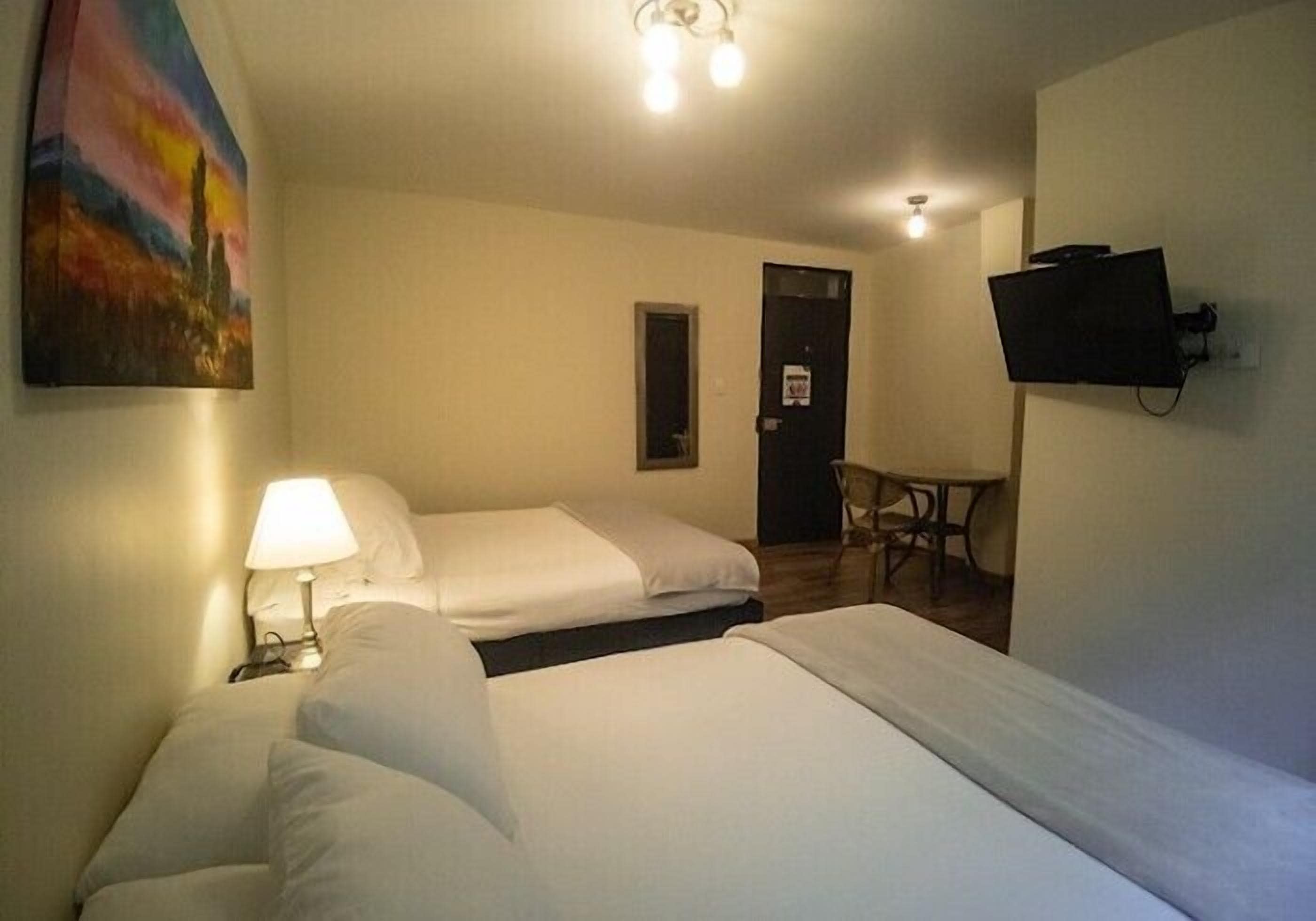 Ein Hotelzimmer mit zwei Betten, einem Schreibtisch, einem Stuhl, einem an der Wand befestigten Fernseher und einer Tür.