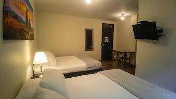 Ein Hotelzimmer mit zwei Betten, einem Schreibtisch, einem Stuhl, einem an der Wand befestigten Fernseher und einer Tür.