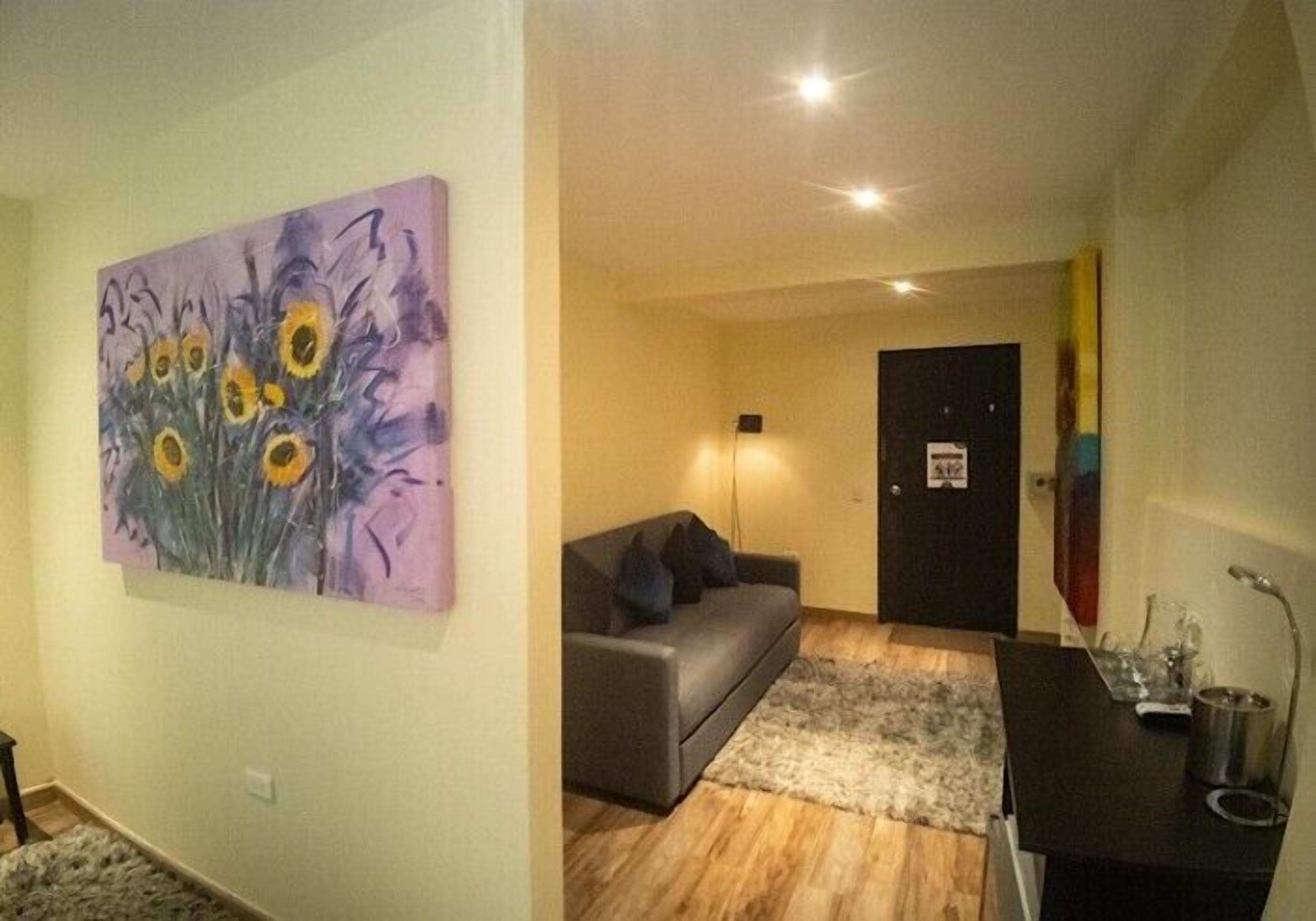 A living room with a gray sofa, a painting of sunflowers, a wooden floor, and a door in the background.