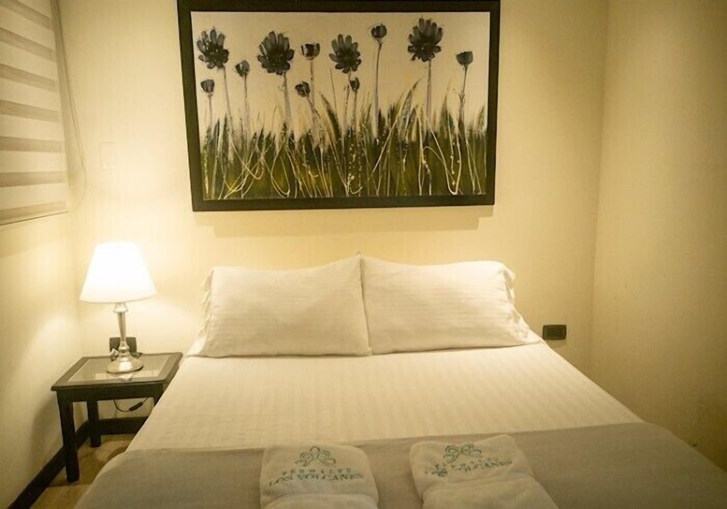 Een hotelkamer met een bed, een nachtkastje met een lamp en een aan de muur hangend schilderij van bloemen.