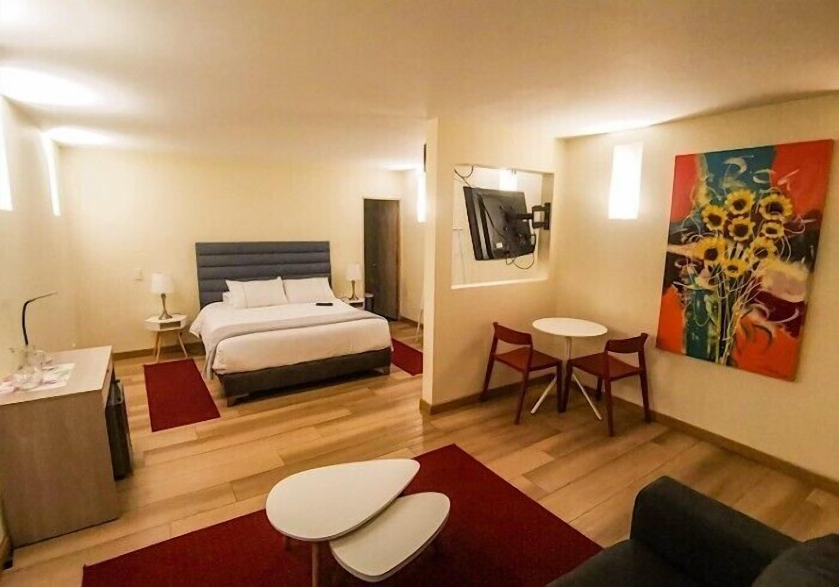 Una habitación de hotel con cama, escritorio, silla, mesita y un cuadro en la pared.