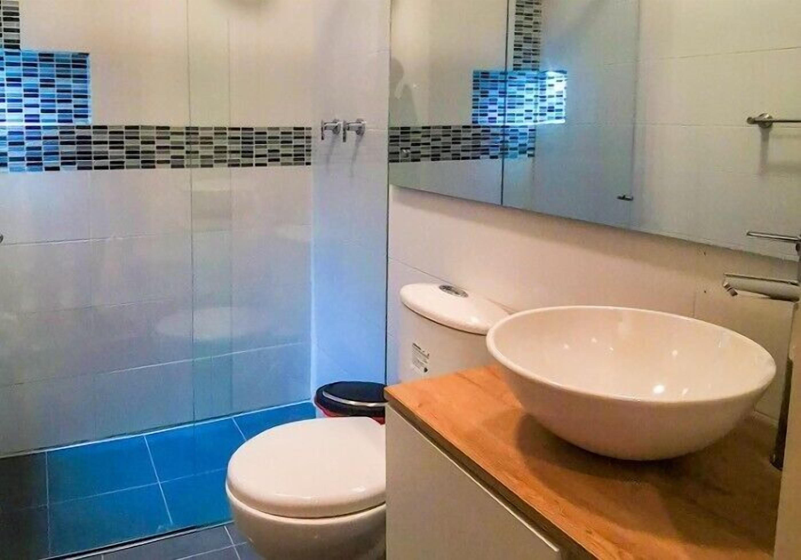 Un baño moderno con inodoro blanco, un lavabo grande de color blanco y zona de ducha con paredes de azulejos azules.