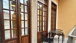 Un balcón con suelo de piedra, puertas de madera y una mesa con sillas.