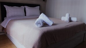 Ein ordentlich bezogenes Bett mit zusammengelegtem Handtuch und zwei Kissen, ein hölzernes Kopfteil und eine schlichte Wand.