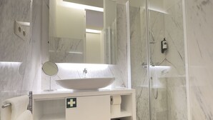 Ein modernes Badezimmer mit Marmorwaschbecken, einem Spiegel, einer Dusche und Holzboden.