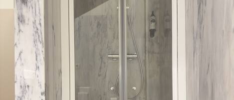 A glass-enclosed shower with a marble wall.