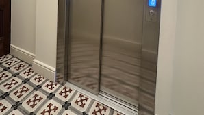 A modern elevator with a digital display, located in a hallway with patterned floor tiles. - Collection 4T in Oporto (Porto)