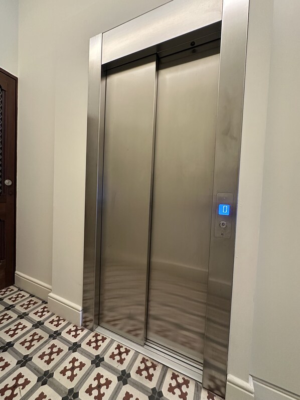 Un ascenseur moderne doté d’un écran numérique, situé dans un couloir dont le sol est recouvert de carreaux décoratifs.