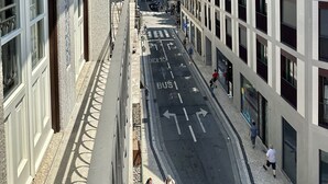 A narrow street with buildings on either side, a clear sky, and a few pedestrians. - Collection 3F in Oporto (Porto)