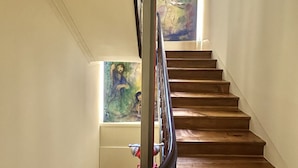 A wooden staircase with a metal handrail, leading to a landing with a large abstract painting. - Collection 4F in Oporto (Porto)