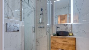 A modern bathroom with a glass-enclosed shower, marble walls, a wooden vanity, and a large mirror.