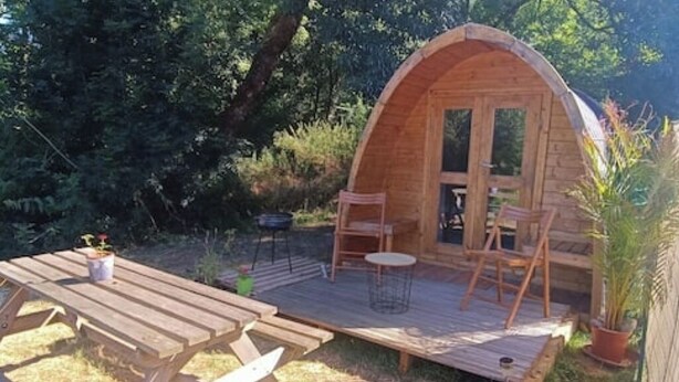 Een houten A-frame hut met een terras, picknicktafel en stoelen.