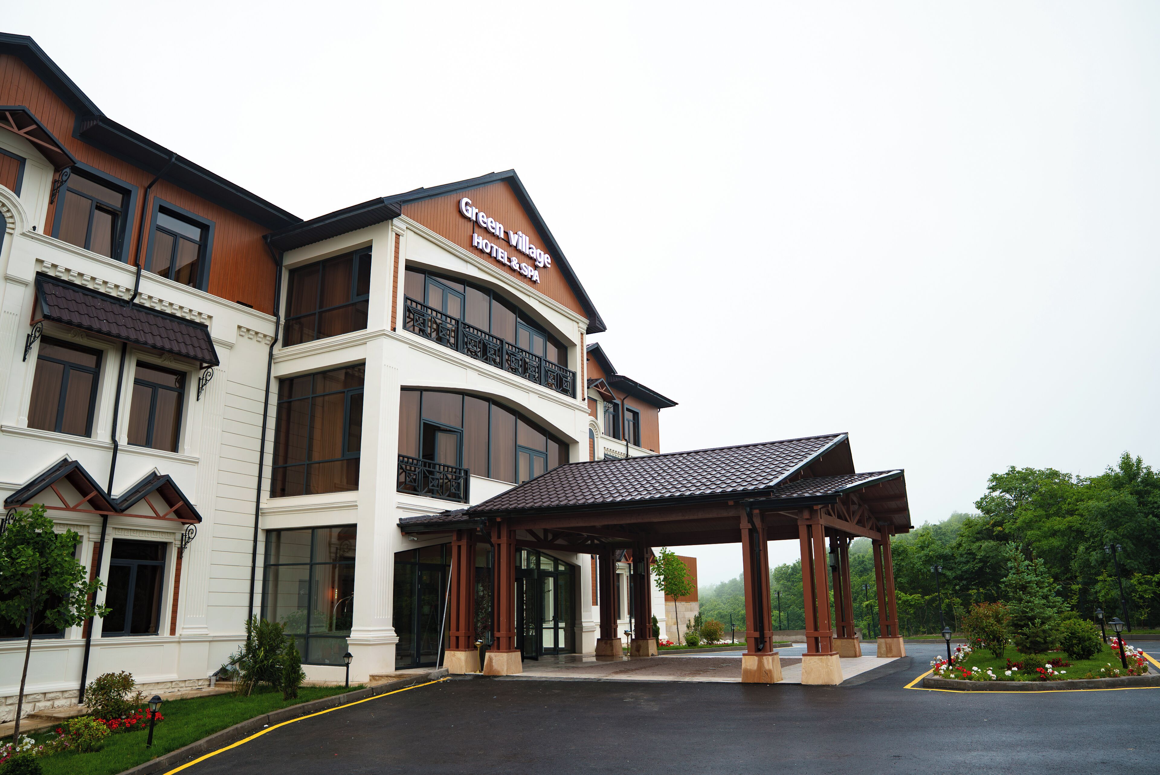 A hotel with a covered entrance, large windows, and a sign reading "Green Village Hotel & Spa".