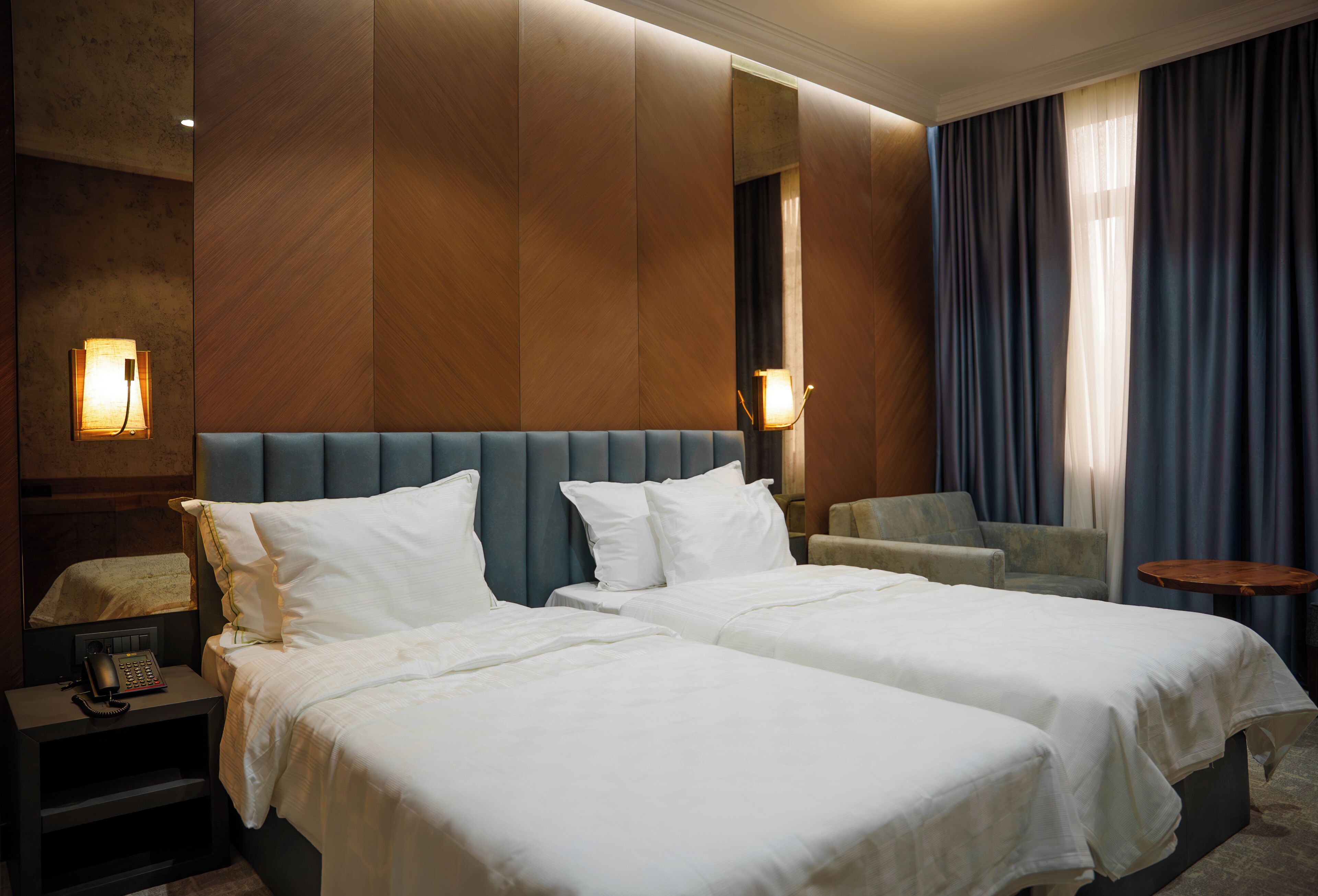 A hotel room with two beds, a nightstand with a telephone, a chair, and a small table.