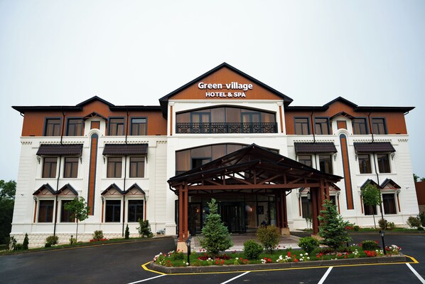 A hotel with a large entrance, a covered waiting area, and a sign reading "Green village HOTEL & SPA".