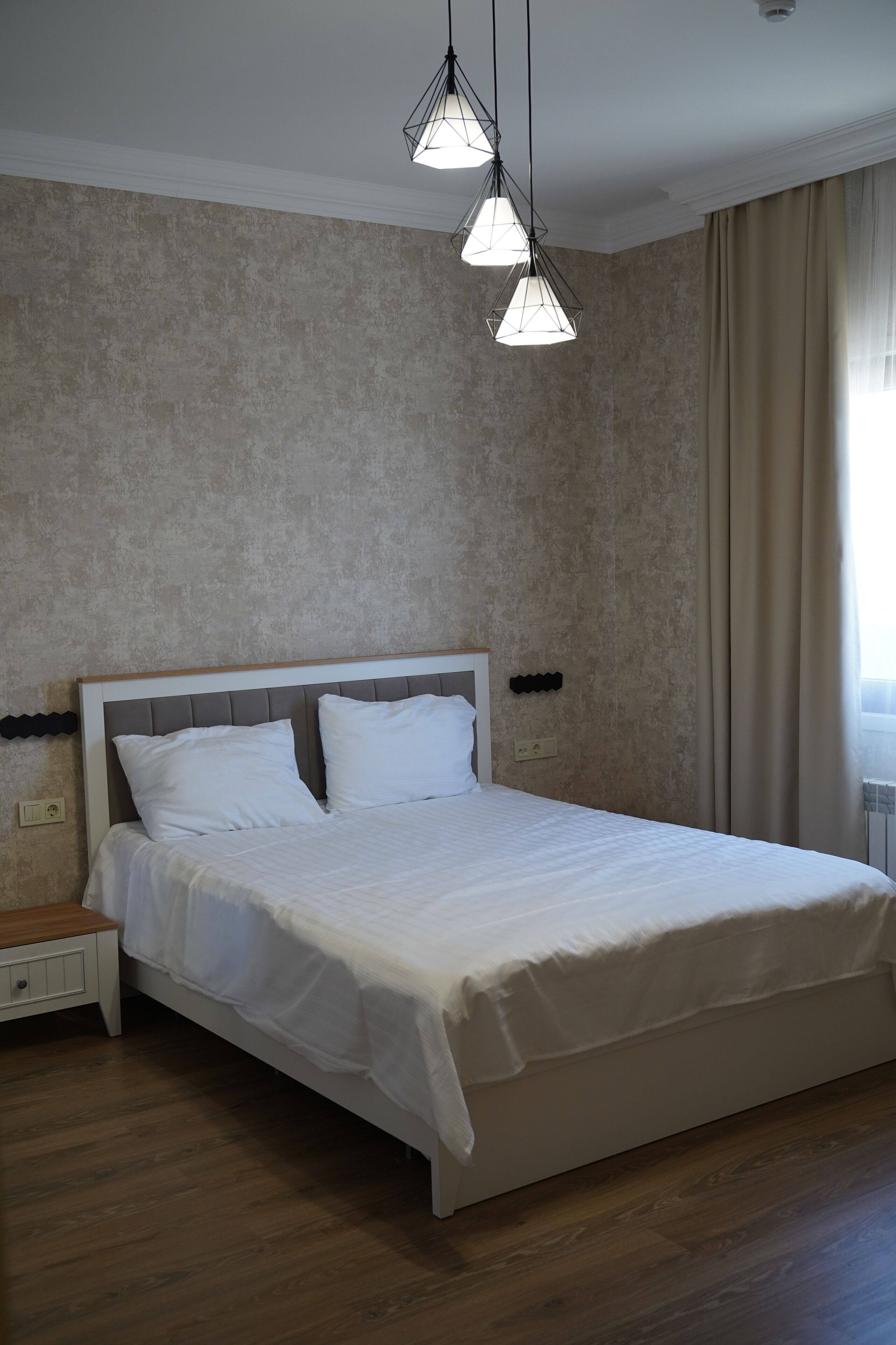 A neatly made bed with white linens, a wooden nightstand, and a textured wall.