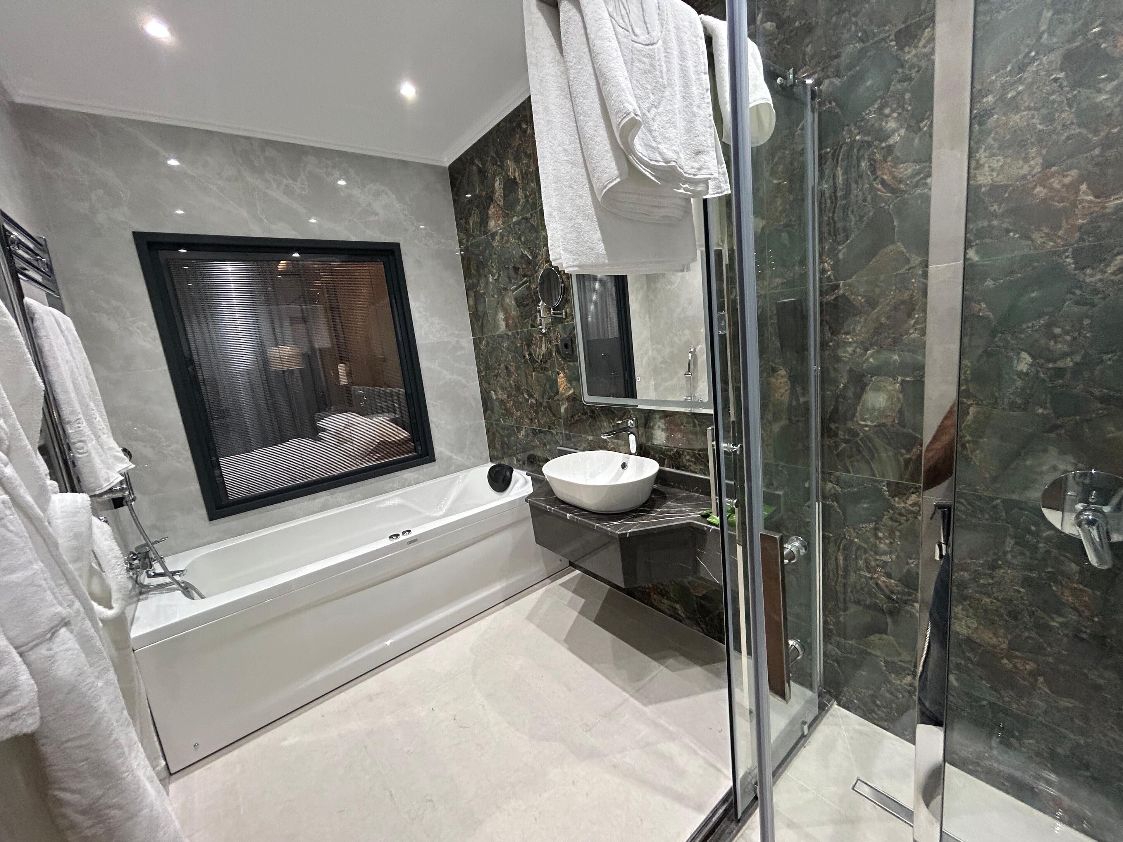 Un baño moderno con bañera, ducha envuelta en vidrio y pared de mármol.