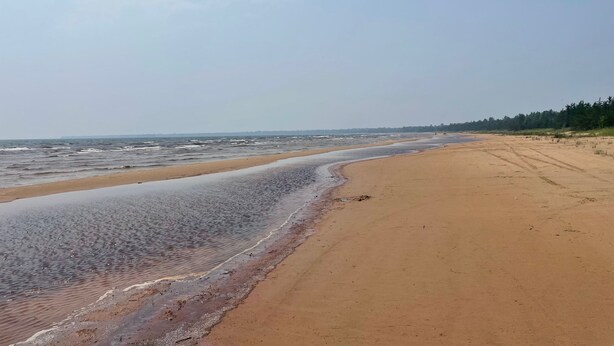 A wide sandy beach with gentle waves, a clear sky, and a distant tree line. - 3-bedroom house in Rexton right on the ATV/snowmobile trails (Naubinway)