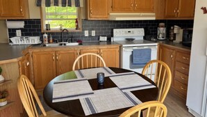 A kitchen with wooden cabinets, a stove, a sink, and a dining table with chairs. - 3-bedroom house in Rexton right on the ATV/snowmobile trails (Naubinway)