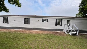 A single-story mobile home with a flat roof, a front porch, and a small attached garage. - 3-bedroom house in Rexton right on the ATV/snowmobile trails (Naubinway)