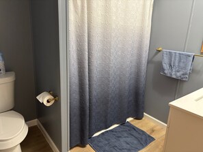 A bathroom with a toilet, a blue shower curtain, a towel rack with a towel, and a small rug on the floor.