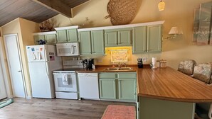 Una cocina con armarios verdes, encimera de madera y lámparas colgantes.