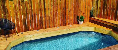 A wooden deck with a swimming pool, surrounded by a wooden fence and a chair.