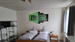 Een slaapkamer met een houten bed, twee nachtkastjes, een zwarte metalen garderobe en een groen abstract kunstwerk aan de muur.