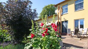 A garden with red flowers and a patio area with outdoor furniture. - Luxuriose Ferienwohnung mit Terrasse, Wiek (Wiek)