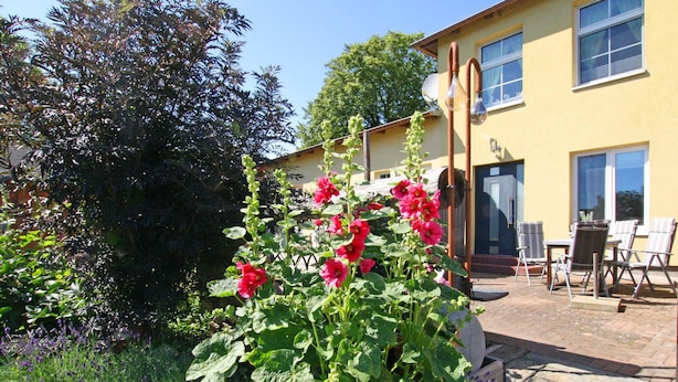 Un jardin agrémenté de fleurs rouges et un espace patio aménagé avec du mobilier d’extérieur.