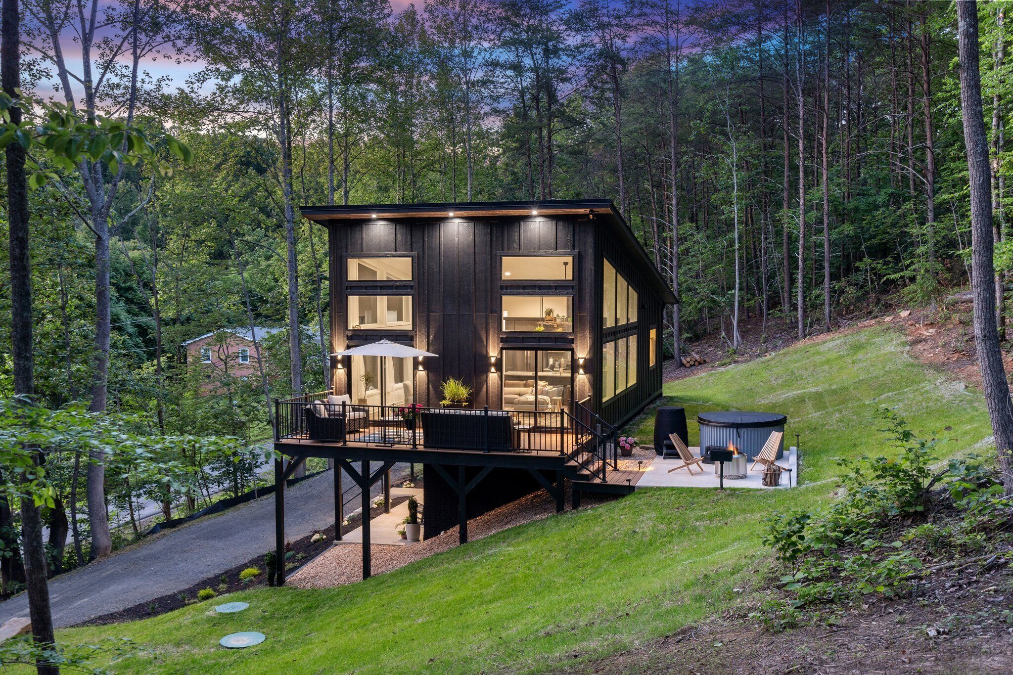 Una cabaña moderna con terraza, ventanas amplias y una zona con fogata.
