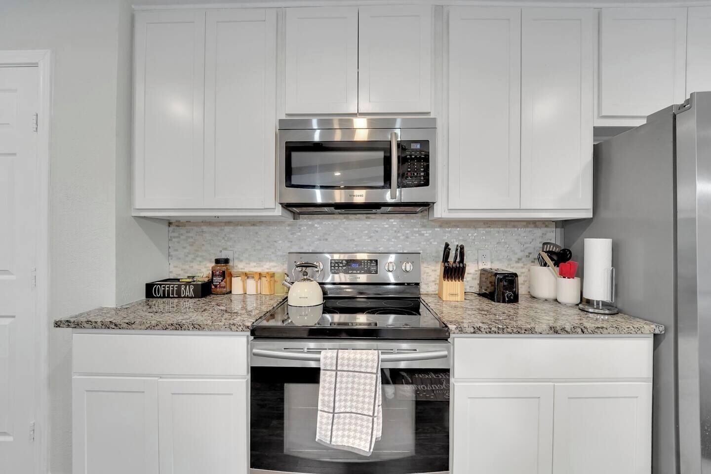 A modern kitchen with white cabinets, stainless steel appliances, and granite countertops.