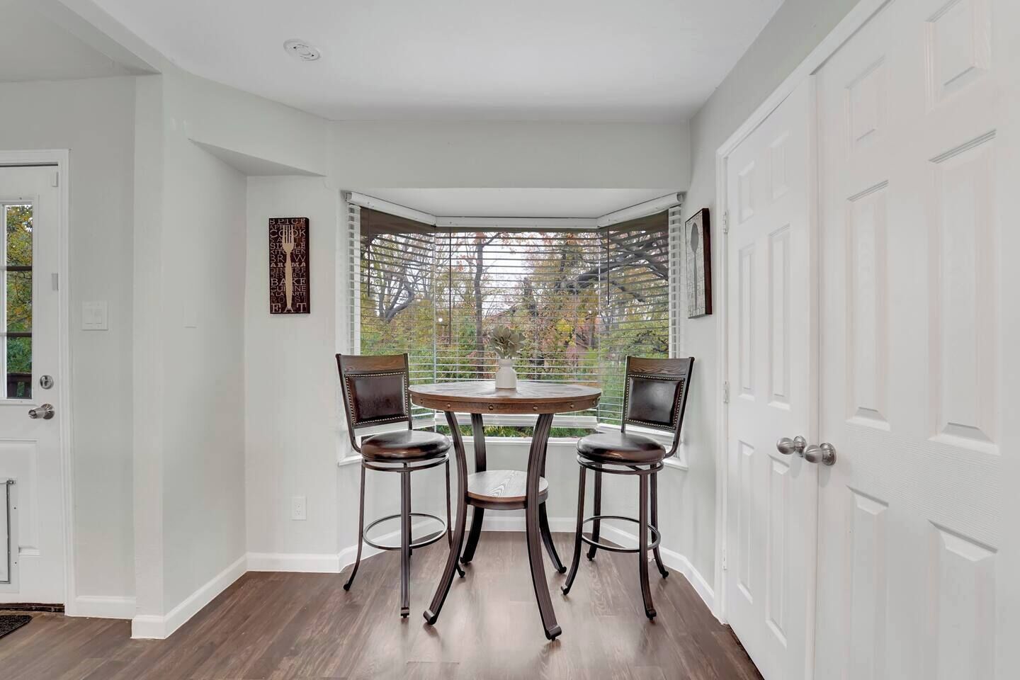 Une pièce d’angle avec une baie vitrée, deux fauteuils, une table et une plante en pot.