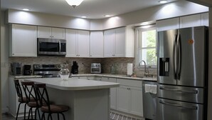 A modern kitchen with white cabinets, stainless steel appliances, a central island with bar stools, and a large refrigerator.