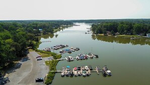 An aerial view of a marina with boats docked along a river, surrounded by dense forest.