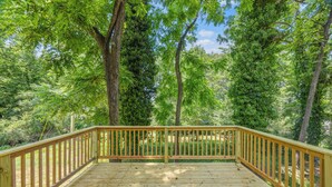Una terraza de madera con barandillas, rodeada de árboles y follaje.