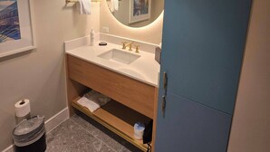 A modern bathroom with a double sink, a round mirror, pendant lights, and a blue cabinet.