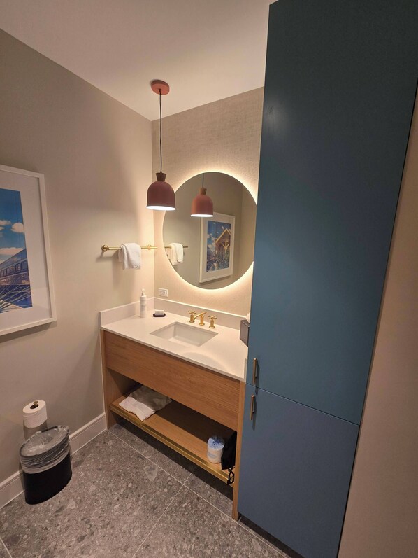 Ein modernes Badezimmer mit einem Doppelwaschbecken, einem runden Spiegel, Pendelleuchten und einem blauen Schrank.