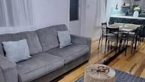 Una sala de estar moderna con un sofá gris, suelo de madera, un tapete estampado y un ventilador de techo.