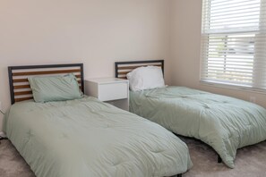 A twin bedroom with two beds, a nightstand, and a window with blinds.