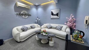 A modern living room with a sectional sofa, a coffee table, decorative pillows, a wall-mounted air conditioner, a floor lamp, and a framed picture. - The Olaya Loft - Self Check-in 1 Bed Apartment (Riyadh)