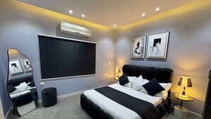 A modern bedroom with a large bed, bedside lamps, a wall-mounted air conditioner, and framed artwork. - The Olaya Loft - Self Check-in 1 Bed Apartment (Riyadh)