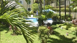 En pool omgivet af frodig vegetation og palmer, med en bygning i baggrunden.