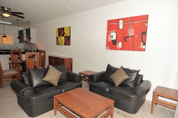 A living room with two black leather sofas, a wooden coffee table, and a red abstract painting on the wall.